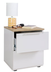 Weißer Nachttisch mit Holzoptik-Oberplatte und zwei Schubladen, obere Schublade halb geöffnet; darauf Tischlampe, Brille, Etui und Buch, Ansicht leicht von vorne links