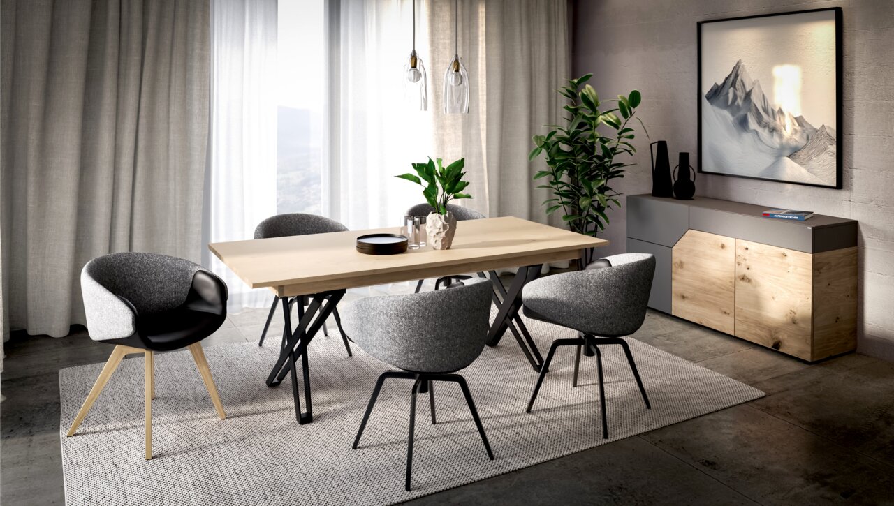 Modernes Esszimmer-Set mit hellem Holztisch und grauen Polsterstühlen auf Teppich, seitliche Perspektive im Raum mit Vorhängen, Pflanzen und Sideboard im Hintergrund.