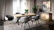 Moderne eetkamerset met een lichte houten tafel en grijze gestoffeerde stoelen op een tapijt, zijaanzicht in de kamer met gordijnen, planten en een dressoir op de achtergrond.