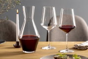 Weinset bestehend aus einer Karaffe und zwei Weingläsern, gefüllt mit Rotwein, auf einem gedeckten Tisch mit Kerze, seitliche Perspektive