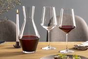 Weinset bestehend aus einer Karaffe und zwei Weingläsern, gefüllt mit Rotwein, auf einem gedeckten Tisch mit Kerze, seitliche Perspektive