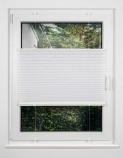 Weiße Plissee-Jalousie an einem Fenster, halb heruntergelassen, mit Blick auf einen Garten. Frontalansicht.