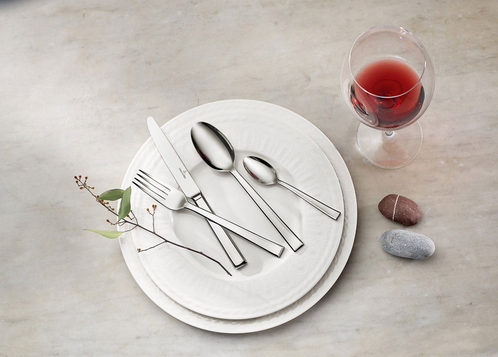 Villeroy & Boch Tafelbesteck 68-tlg. VICTOR Elegantes Tafelbesteck-Set auf einem weißen Teller, mit einem Weinglas und dekorativen Steinen, aus der Vogelperspektive fotografiert.