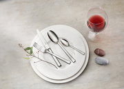 Elegantes Tafelbesteck-Set auf einem weißen Teller, mit einem Weinglas und dekorativen Steinen, aus der Vogelperspektive fotografiert.