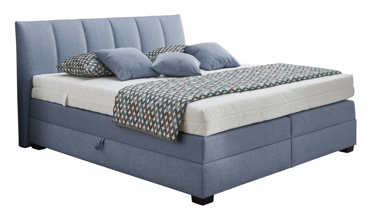 Boxspringbett in blauer Farbe mit gestepptem Kopfteil, seitlicher Perspektive, dekoriert mit gemusterten Kissen und Decke.