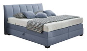 Boxspringbett in blauer Farbe mit gestepptem Kopfteil, seitlicher Perspektive, dekoriert mit gemusterten Kissen und Decke.