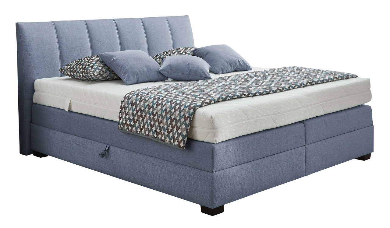 Boxspringbett in blauer Farbe mit gestepptem Kopfteil, seitlicher Perspektive, dekoriert mit gemusterten Kissen und Decke.