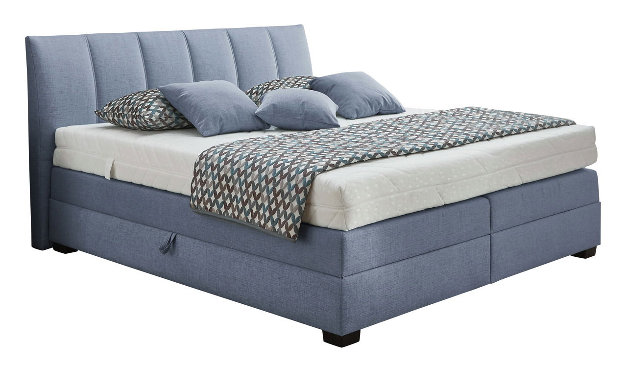 Boxspringbett in blauer Farbe mit gestepptem Kopfteil, seitlicher Perspektive, dekoriert mit gemusterten Kissen und Decke.