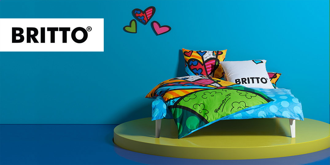 Ein Bett im Britto-Design mit leuchtenden Kissen, die vor einer hellblauen Wand stehen.