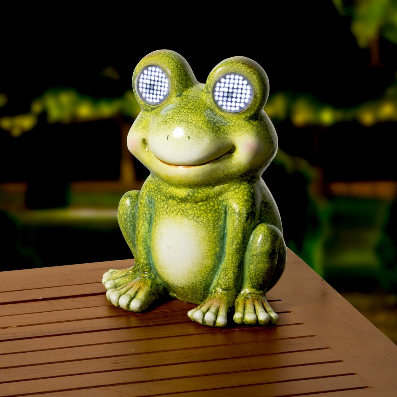 Solarbetriebener Frosch aus Polyresin mit leuchtenden Augen, auf einem Tisch im Freien platziert, frontal fotografiert.
