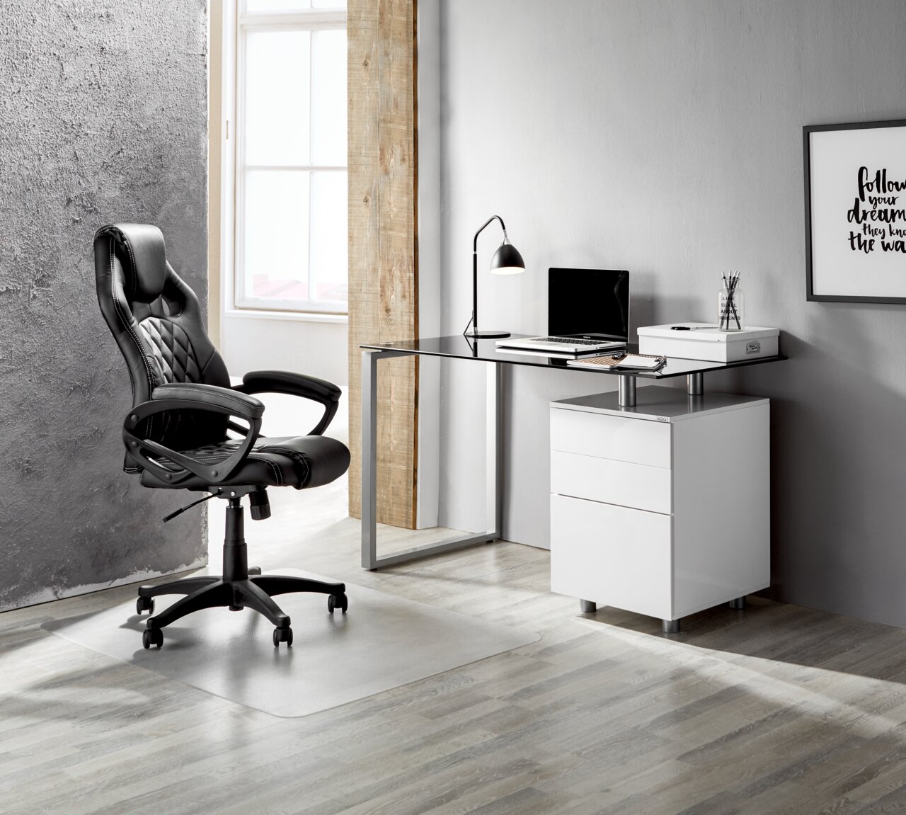 Moderner Schreibtisch mit Glasplatte und weißem Unterschrank, seitliche Perspektive, neben einem schwarzen Bürostuhl in einem stilvollen Raum.