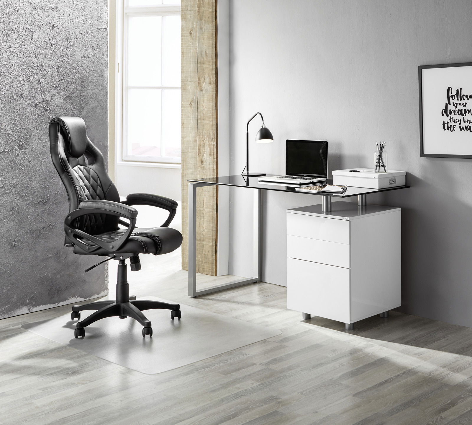 Moderner Schreibtisch mit Glasplatte und weißem Unterschrank, seitliche Perspektive, neben einem schwarzen Bürostuhl in einem stilvollen Raum.