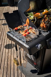 Gasgrill Allflame Hero 4 in seitlicher Perspektive mit gegrilltem Gemüse und Fleischspießen auf dem Rost, umgeben von Grillzubehör.