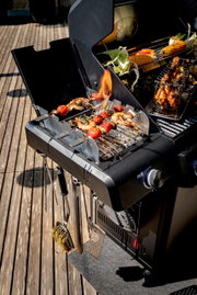 Gasgrill Allflame Hero 4 in seitlicher Perspektive mit gegrilltem Gemüse und Fleischspießen auf dem Rost, umgeben von Grillzubehör.
