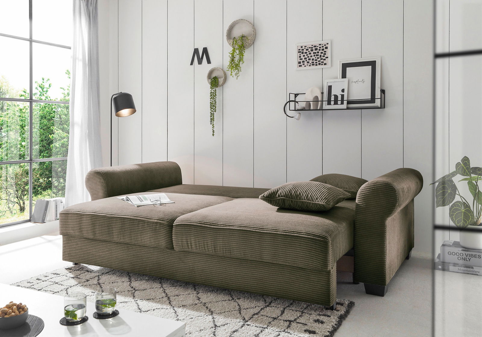 Funktionssofa in einem modernen Wohnzimmer, seitliche Perspektive, mit grüner Polsterung und dekorativen Kissen.