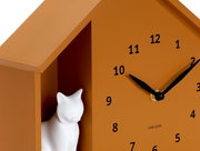 Nahaufnahme einer orangefarbenen Wanduhr mit schwarzem Zifferblatt und Zeigern, sowie einer weißen Katzenfigur in einem seitlichen Fach.