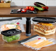 Vakuumier-Set EASYFRESH, 5-tlg, bestehend aus Vakuumpumpe, Frischhalteboxen und Beuteln, auf einer Küchenarbeitsplatte präsentiert, mit frischen Lebensmitteln wie Lachs, Basilikum und Karotten, seitliche Perspektive.