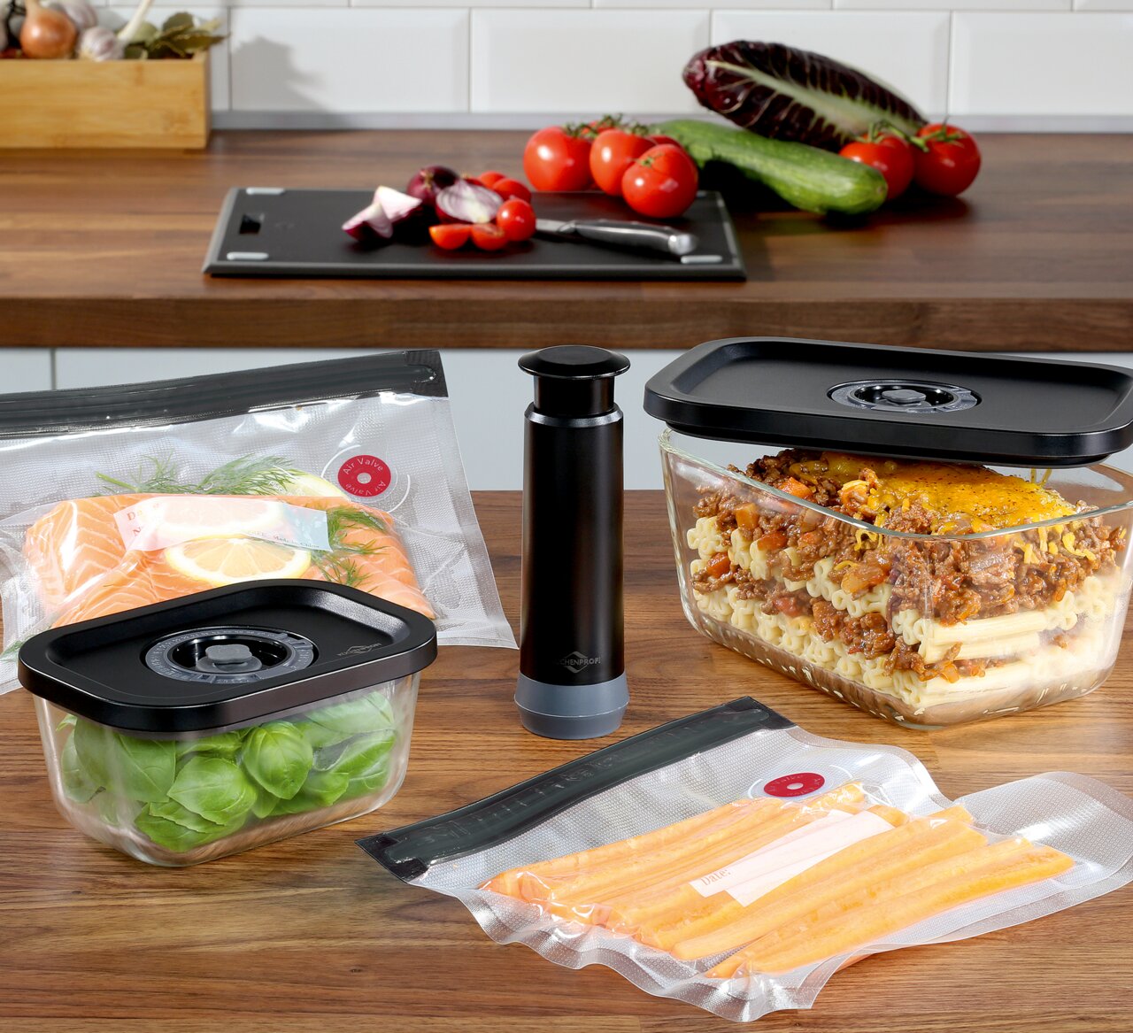 Vakuumier-Set EASYFRESH, 5-tlg, bestehend aus Vakuumpumpe, Frischhalteboxen und Beuteln, auf einer Küchenarbeitsplatte präsentiert, mit frischen Lebensmitteln wie Lachs, Basilikum und Karotten, seitliche Perspektive.