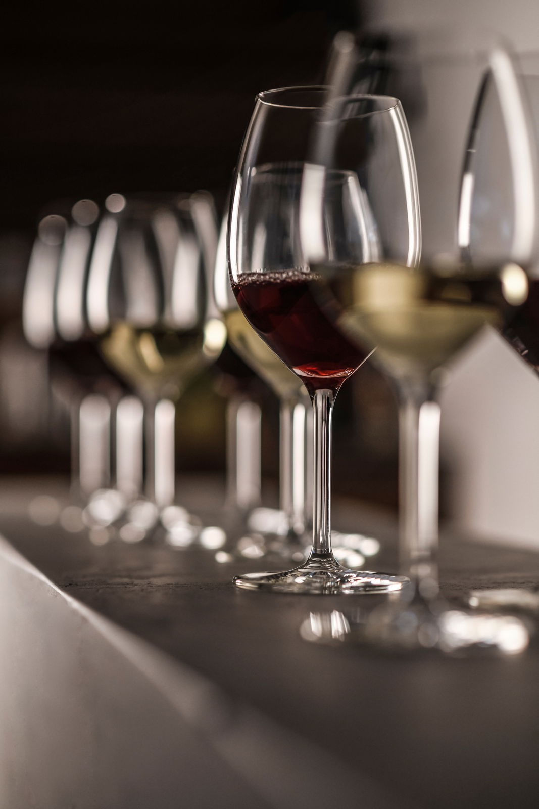 SCHOTT ZWIESEL Weißweinglas-Set 4-tlg For You Eine Reihe von Weißweingläsern, teilweise gefüllt mit Rot- und Weißwein, auf einer Theke aus seitlicher Perspektive.