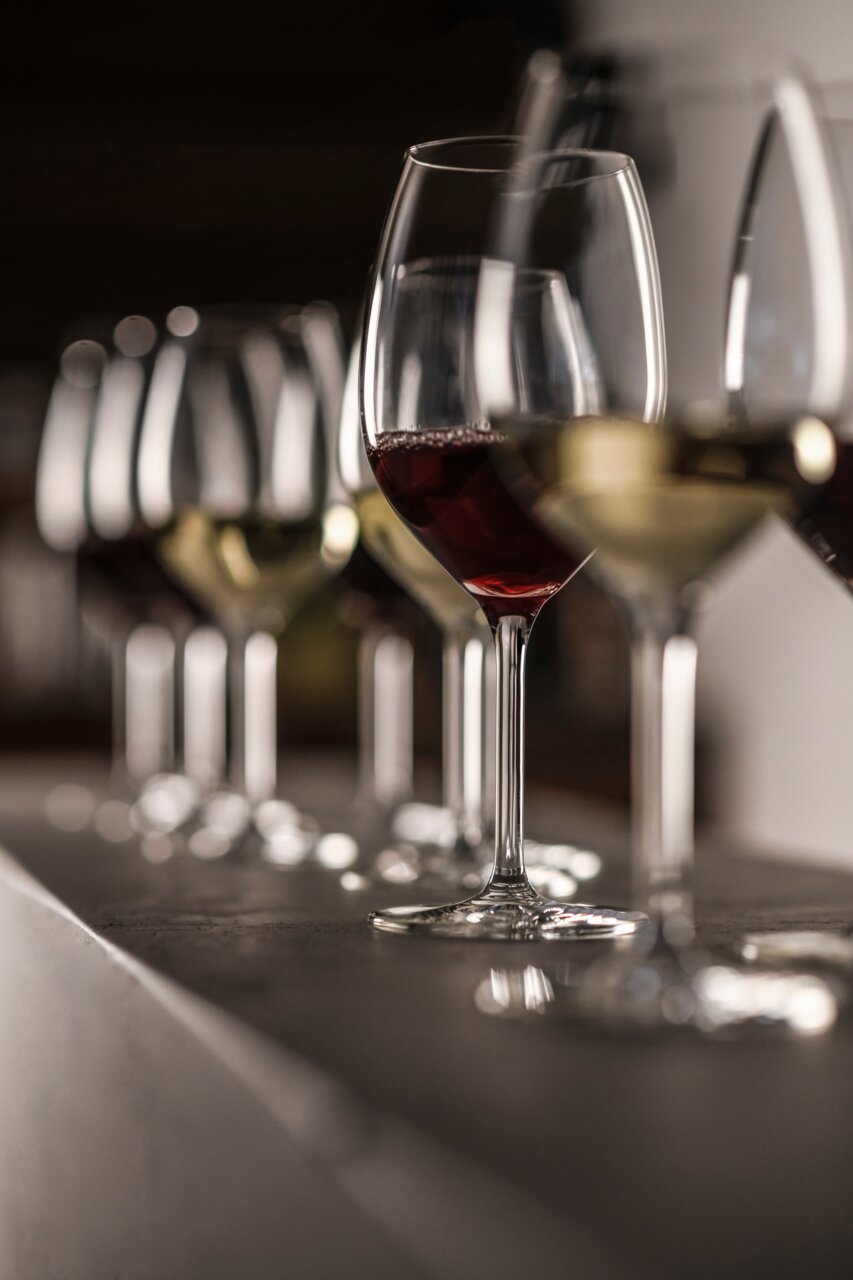 SCHOTT ZWIESEL Weißweinglas-Set 4-tlg For You Eine Reihe von Weißweingläsern, teilweise gefüllt mit Rot- und Weißwein, auf einer Theke aus seitlicher Perspektive.