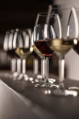 Eine Reihe von Weißweingläsern, teilweise gefüllt mit Rot- und Weißwein, auf einer Theke aus seitlicher Perspektive.