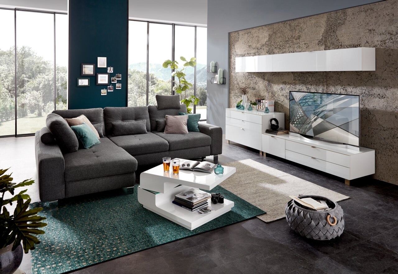 Modernes Wohnzimmer mit grauem Ecksofa, weißem Couchtisch und TV-Lowboard in einer stilvollen, hellen Umgebung. Perspektive von vorne.