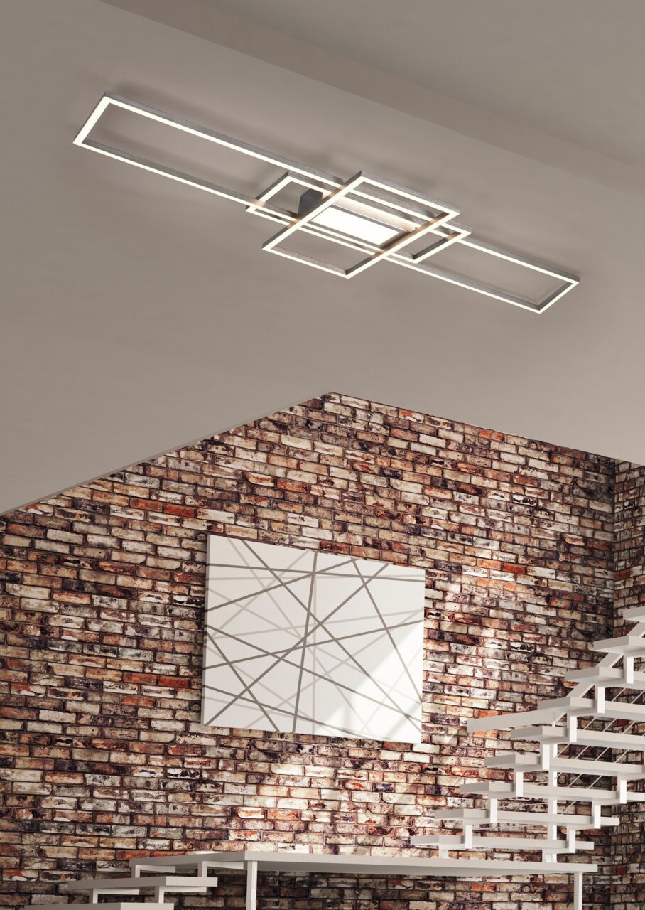Moderne LED-Deckenleuchte mit geometrischem Design, montiert an einer Decke in einem Raum mit Backsteinwand, aus seitlicher Perspektive betrachtet.