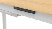 Detailansicht aus leicht schräger Unterseiten-Perspektive: schwarzes Bedienpanel eines höhenverstellbaren Schreibtischs unter einer Holzplatte mit Tasten für Auf/Ab und Speicherplätzen 1–3 sowie M