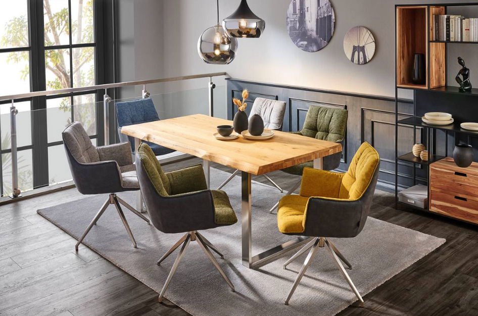 Esszimmer mit modernem Holztisch und Metallgestell, umgeben von bunten Drehstühlen, aus der Perspektive eines offenen Wohnbereichs fotografiert.