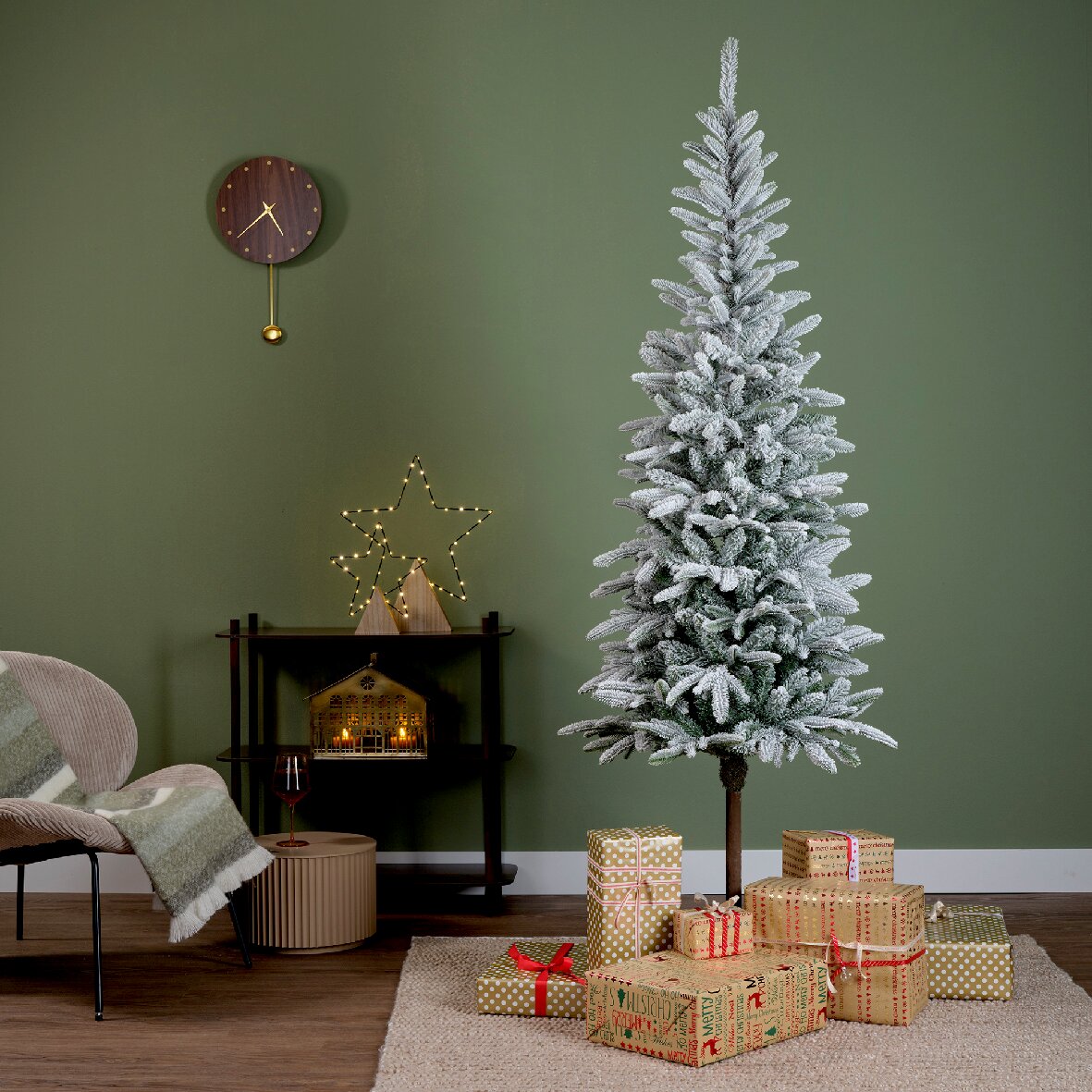 Künstlicher Weihnachtsbaum Alpbach Tanne mit Schnee-Effekt, umgeben von Geschenken, in einem gemütlich dekorierten Raum, seitliche Perspektive