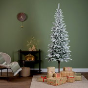 Künstlicher Weihnachtsbaum Alpbach Tanne mit Schnee-Effekt, umgeben von Geschenken, in einem gemütlich dekorierten Raum, seitliche Perspektive