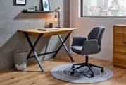 Moderner Schreibtisch mit Holzplatte und schwarzen Metallbeinen, seitliche Perspektive, neben einem grauen Bürostuhl auf einem runden Teppich.