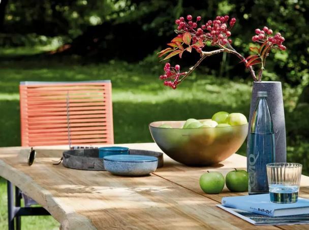 Holz-Esstisch im Freien mit Dekorationen wie einer Schale mit grünen Äpfeln, einer Vase mit roten Beeren und Geschirr, seitliche Perspektive