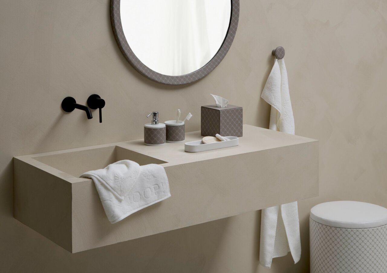 JOOP! Becher CORNFLOWER Moderner Badezimmerbecher aus Porzellan in Weiß und Grau, auf einem Waschbecken neben einem Seifenspender und einer Zahnbürste, aus seitlicher Perspektive fotografiert.