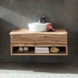 Moderner Waschtisch aus Holz mit integriertem Waschbecken, frontal fotografiert. Unter dem Waschbecken befinden sich offene Regalfächer mit Handtüchern und Accessoires.
