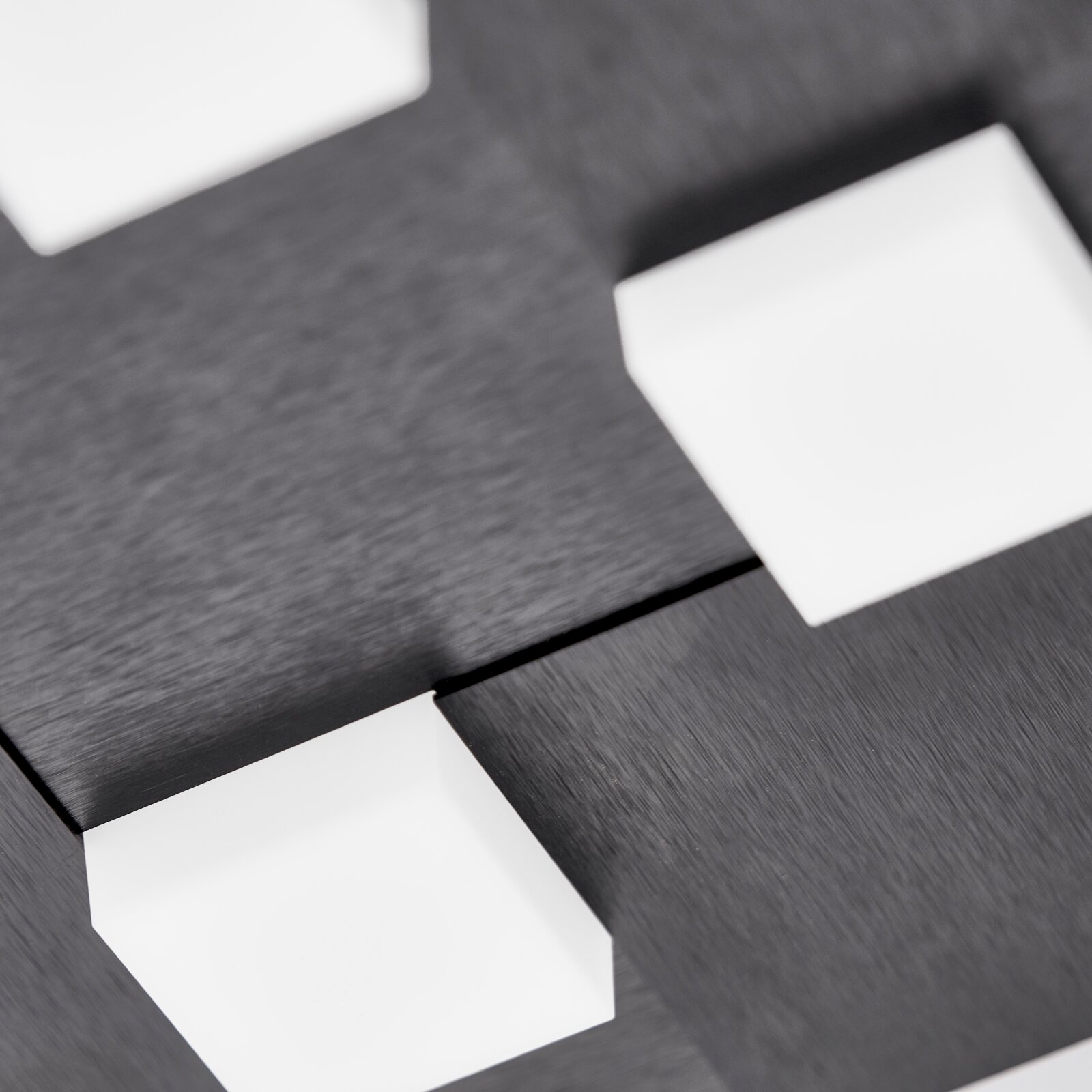Nahaufnahme aus schräger Perspektive einer modernen Deckenleuchte mit gebürsteter schwarzer Metalloberfläche und quadratischen weißen Leuchtelementen
