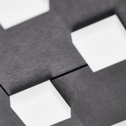 Nahaufnahme aus schräger Perspektive einer modernen Deckenleuchte mit gebürsteter schwarzer Metalloberfläche und quadratischen weißen Leuchtelementen
