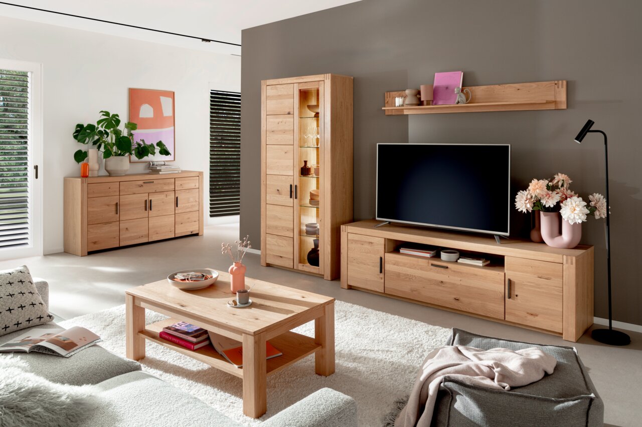 Modernes Wohnzimmer mit einem TV-Element aus Holz, frontal betrachtet. Das TV-Element steht vor einer grauen Wand und ist mit einem Fernseher, Dekorationen und Blumen geschmückt.