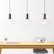 Drei moderne Hängeleuchten aus Glas über einem Esstisch, seitliche Perspektive