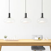 Drei moderne Hängeleuchten aus Glas über einem Esstisch, seitliche Perspektive