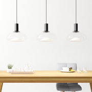 Drie moderne glazen hanglampen boven een eettafel, zijaanzicht