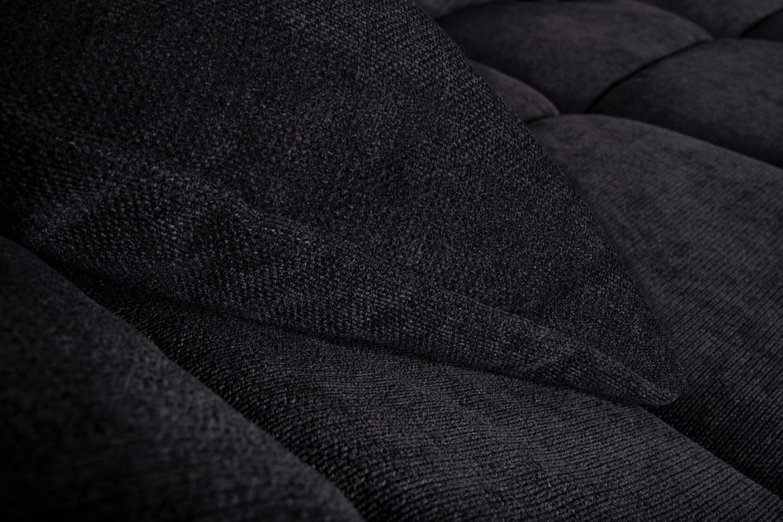 Nahaufnahme einer dunkelgrauen, strukturierten Stoffoberfläche eines Sofas mit Kissen, seitliche Perspektive.