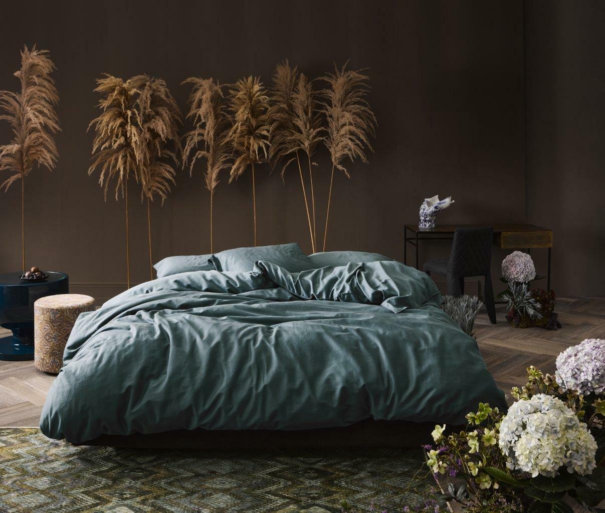 Luxuriöse Bettwäsche in einem stilvoll eingerichteten Schlafzimmer mit Pflanzen und eleganten Möbeln, aus der Perspektive von vorne betrachtet.