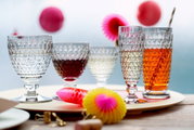 Verschiedene Villeroy & Boch Gläser der Boston Kollektion auf einem Tisch, von links nach rechts: Wasserglas, Rotweinglas, Weissweinglas, Sektglas und Longdrinkglas, mit dekorativen Elementen im Hintergrund. Perspektive: seitlich.