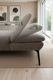 Moderne grijze stoffen bank met verstelbare rugleuning en zwarte metalen poten in een lichte woonkamer, close-up van opzij vanuit een licht schuin perspectief van rechts.