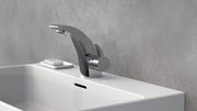 Moderne Waschtischarmatur aus Chrom in seitlicher Perspektive, montiert auf einem weißen Waschbecken vor einer grauen Wand.