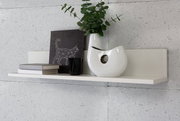 Modernes weißes Wandregal mit Dekoration, darunter Bücher, eine Vase mit Pflanzen und ein Kunstwerk, seitliche Perspektive.