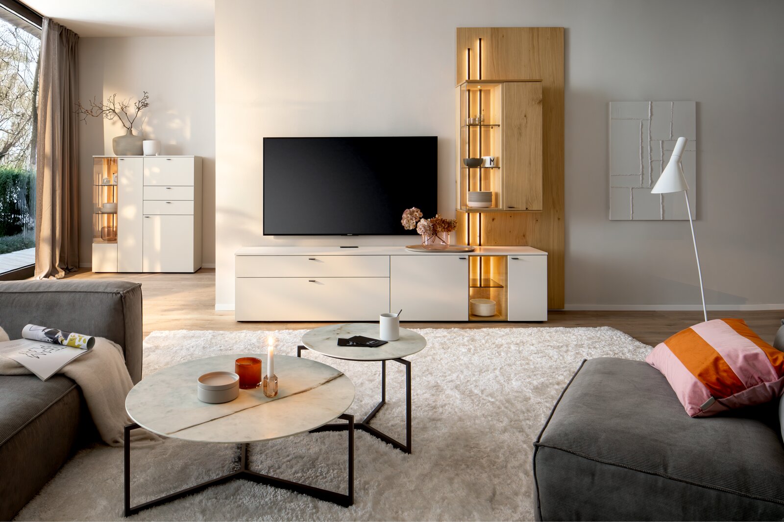 Moderne Wandkombination VANYA von Venjakob in einem stilvollen Wohnzimmer, frontal betrachtet. Die Kombination aus Holz- und Weißtönen bietet Stauraum und dekorative Beleuchtung.