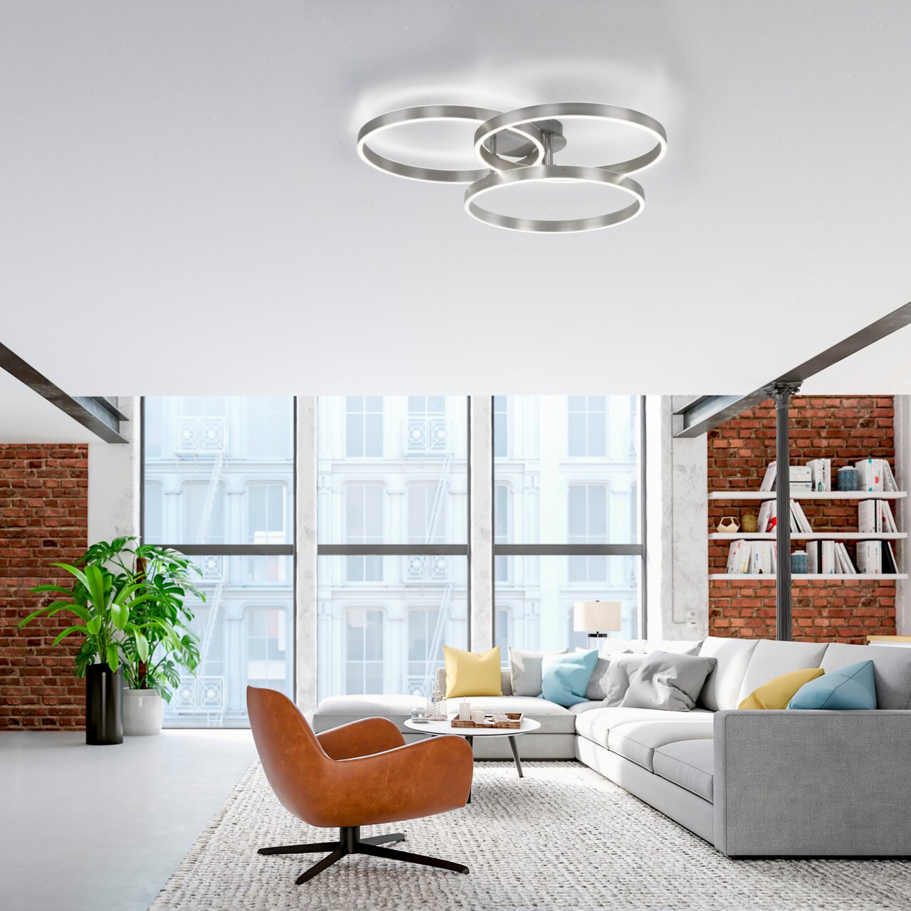 Moderne Deckenleuchte aus Stahl mit drei ineinander verschlungenen Ringen, von unten betrachtet in einem stilvollen Wohnzimmer mit großen Fenstern und Backsteinwänden.