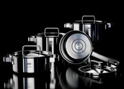 Set aus vier glänzenden Edelstahlkochtöpfen und einer Pfanne mit Deckeln, auf schwarzem Hintergrund präsentiert, aus seitlicher Perspektive.